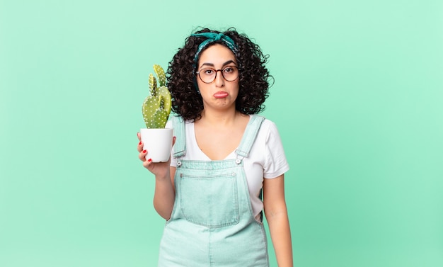 Bella donna araba che si sente triste e piagnucolona con uno sguardo infelice e piange e tiene in mano un cactus in vaso