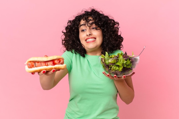 Foto donna abbastanza araba che tiene un'insalata e un hot dog. concetto di dieta