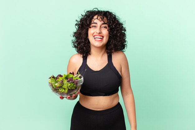 Pretty arab woman looking happy and pleasantly surprised and holding a salad. diet concept