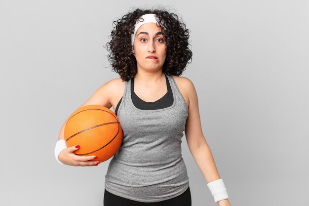 Pretty arab woman looking puzzled and confused and holding a basketball ball. sport concept