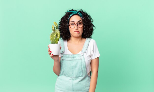 Bella donna araba che sembra perplessa e confusa e tiene in mano un cactus in vaso