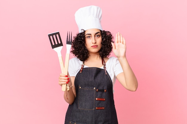 Donna abbastanza araba che sembra seria mostrando palmo aperto che fa gesto di arresto. concetto di chef barbecue