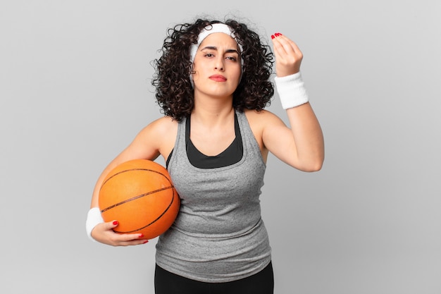 Pretty arab woman making capice or money gesture, telling you\
to pay and holding a basketball ball. sport concept