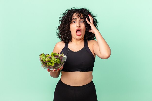 Pretty arab woman screaming with hands up in the air and holding a salad. diet concept