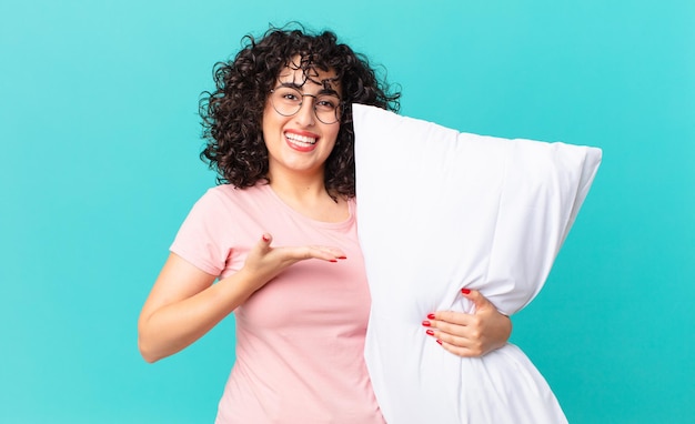 Pretty arab woman smiling cheerfully, feeling happy and showing a concept. wearing pajamas and holding a pillow