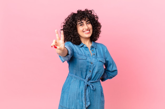 Pretty arab woman smiling and looking happy, gesturing victory or peace