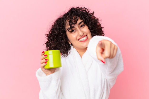 Pretty arab woman wearing bathrobe and holding a conditioner product