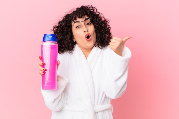 Pretty arab woman wearing bathrobe and holding a shampoo bottle