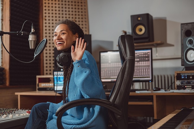 Pretty archorwoman radio presenter greeting while talking into\
microphone in a broadcasting and sound recording studio