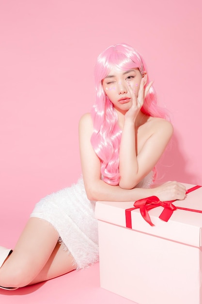 Pretty Asian beautiful woman model long hair with fancy makeup on face and perfect skin with gift box on isolated pink background Facial treatment Cosmetology plastic surgery