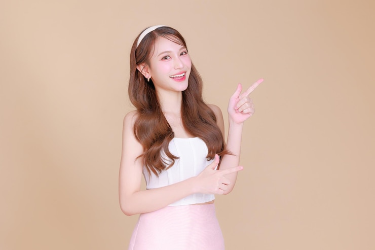 美麗的亞洲美女, 卷曲的長髮, 韓國化<unk>, 發光的臉和健康的面部皮膚, 肖像笑容, 指向複製空間在孤立的<unk>色背景, 化<unk>美容, 整形外科