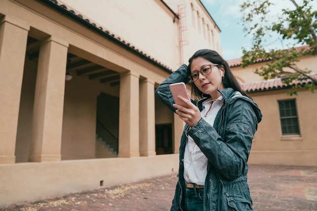 симпатичная азиатская женщина просматривает телефон и спокойно стоит в красивом здании.