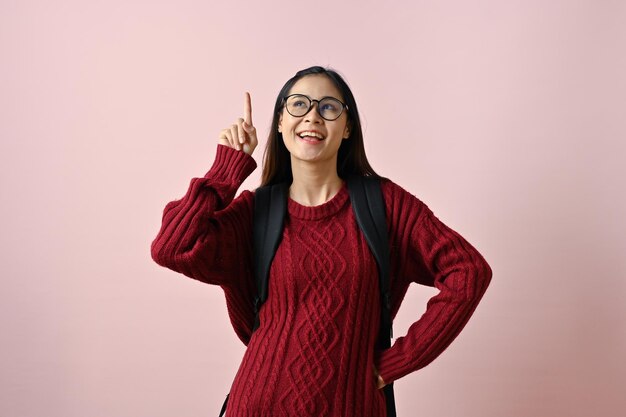 Симпатичная азиатская студентка колледжа смотрит и указывает пальцем на совет или рекомендацию жеста