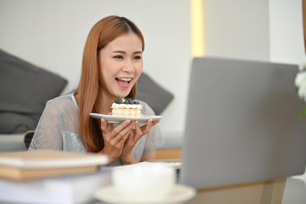 彼女のオンラインフォロワーにおいしいケーキをレビューしているカフェのかなりアジアの女性の食品ブロガー