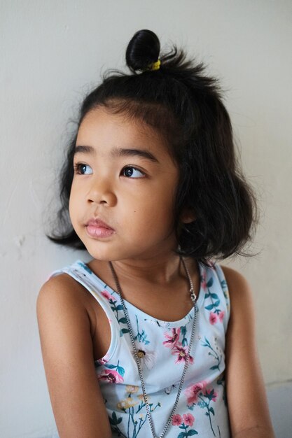 Довольно азиатский маленький ребенок, глядя на свет с белой стеной в качестве фона