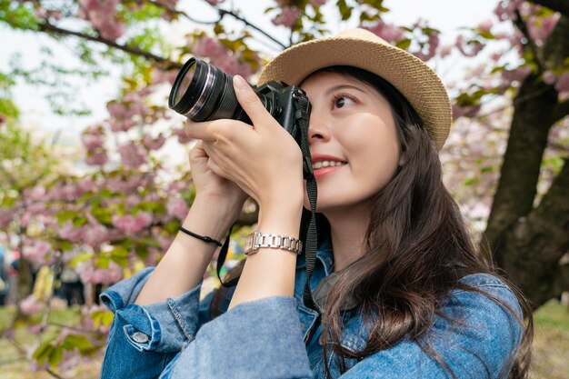 pretty asian visitor filming photo or video and looking happy with a background of plant in japan.
