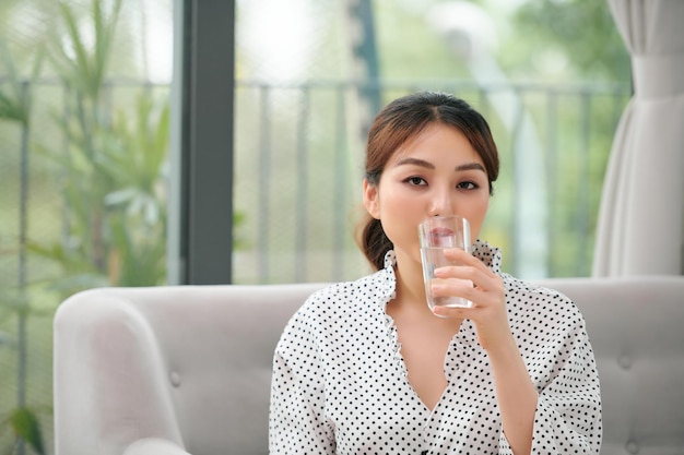 Pretty asian woman drinking water on couch at home in the living room