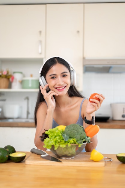 かわいいアジア人の女性が朝食の準備をしながら音楽を楽しみながらカメラに向かって微笑んでいる
