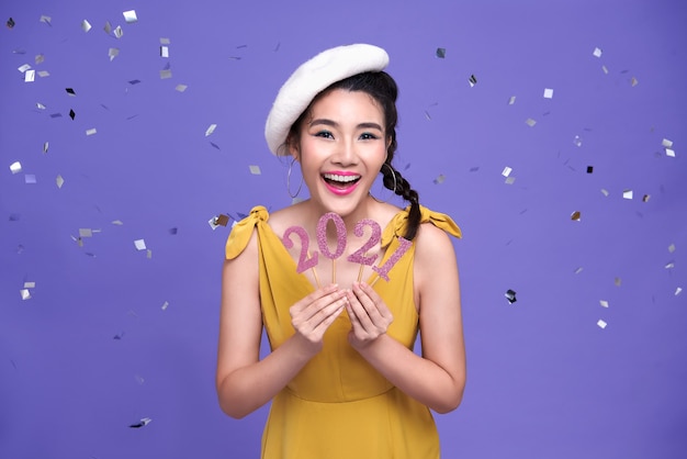 Pretty asian woman smile  welcoming the new year 2021with silver confetti party on bright purple wall.