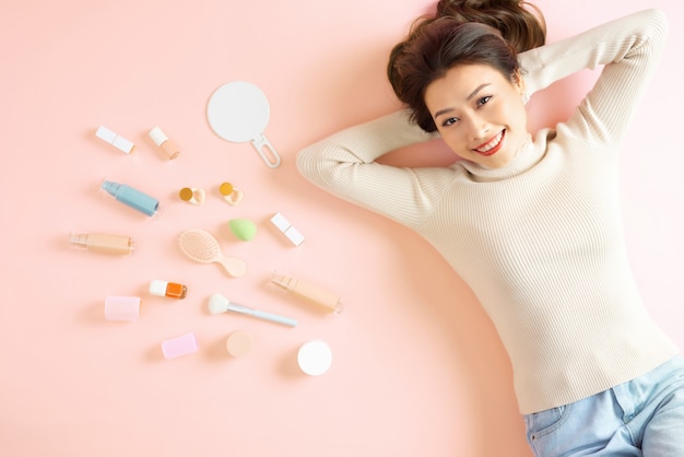 Pretty Asian woman smiling while lying on pink floor with her cosmetic makeup tools