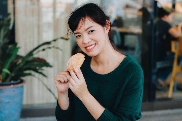 Photo pretty asian woman wearing green sweater and enjoyed eating japanese puff creamshu cream