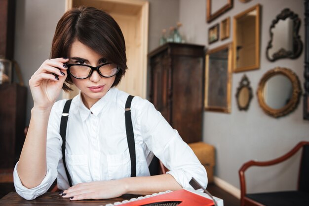 Pretty authoress in glasses and white shirt sitting by the table