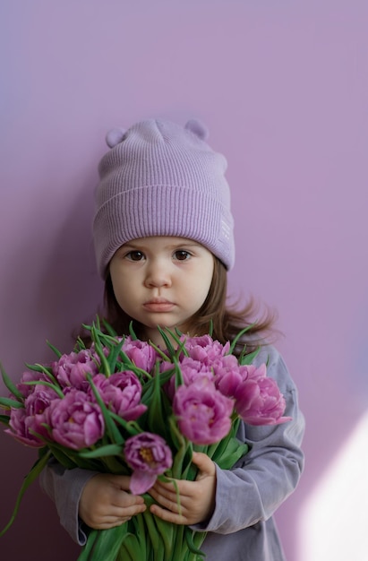 Photo pretty baby toddler wearing purple with bouquet of tulips