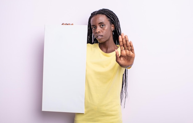 Pretty black woman looking serious showing open palm making stop gesture. blank canvas concept