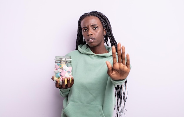 pretty black woman looking serious showing open palm making stop gesture. jelly candies concept