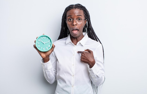 pretty black woman looking shocked and surprised with mouth wide open, pointing to self. alarm clock concept