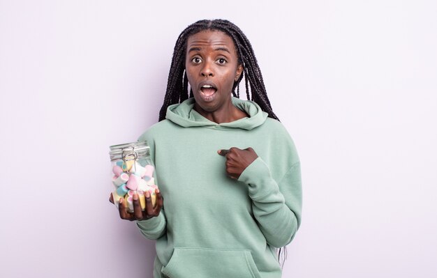 Pretty black woman looking shocked and surprised with mouth wide open, pointing to self. jelly candies concept