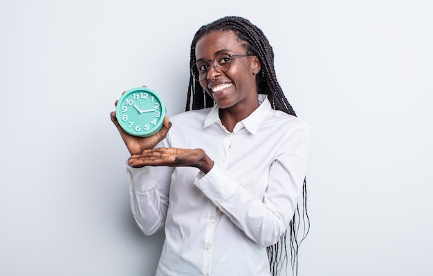 Pretty black woman smiling cheerfully feeling happy and showing a concept alarm clock concept
