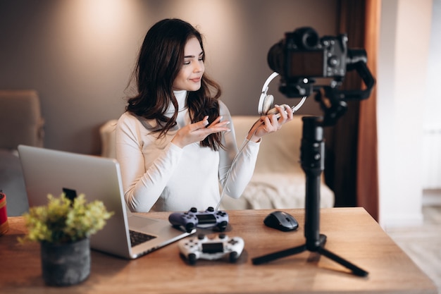 Pretty blogger woman is filming and showing her preference in headphones for video games. Influencer young woman live streaming.