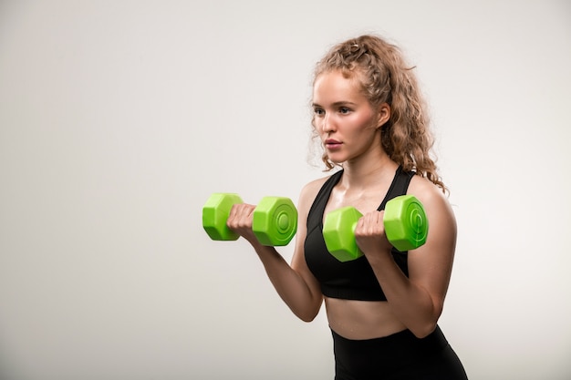 Pretty blond fit girl with curly hair doing exercise for arm muscles with dumbbells during workout