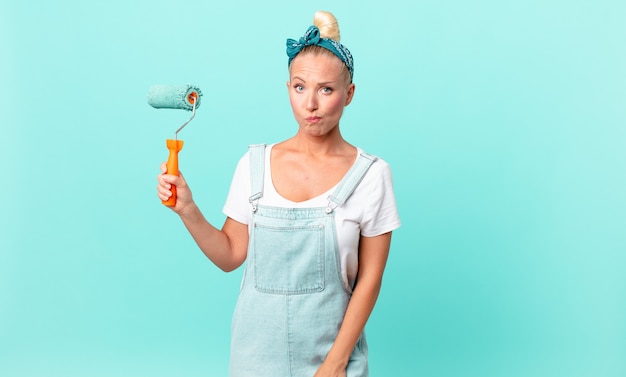 Pretty blond woman feeling sad, upset or angry and looking to the side and painting a wall