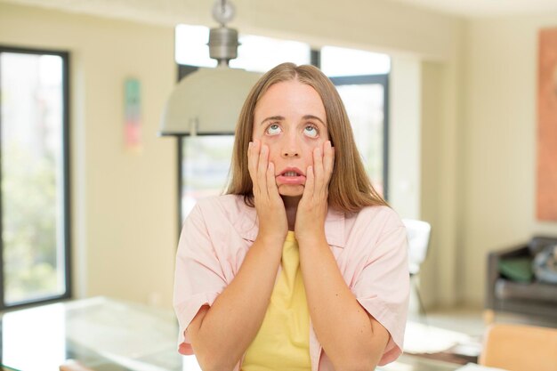 pretty blond woman feeling shocked and scared looking bored with hands on cheeks