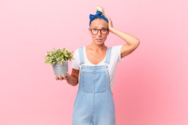 pretty blond woman feeling stressed, anxious or scared, with hands on head and holding a plant