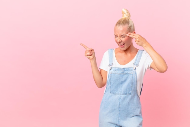 Pretty blond woman looking unhappy and stressed, suicide gesture making gun sign