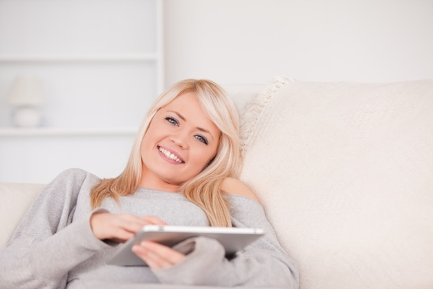 Pretty blond woman lying on a sofa relaxing on a line of tablet computers