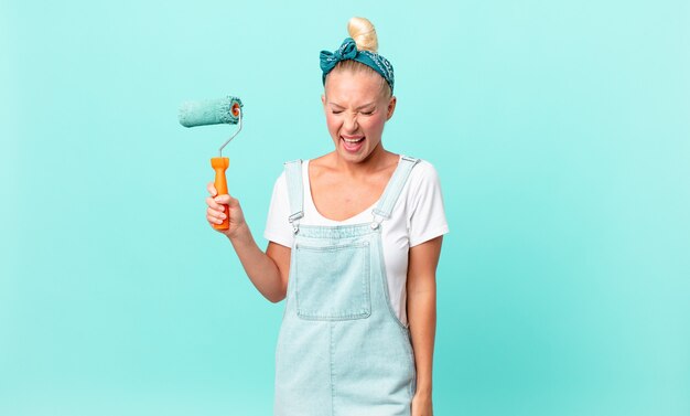 Pretty blond woman shouting aggressively, looking very angry and painting a wall