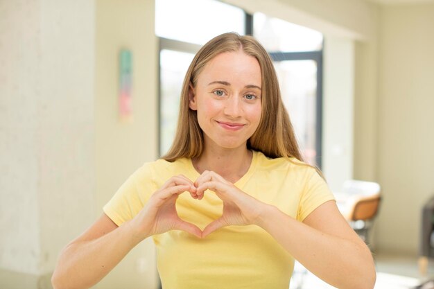 写真 かなり金髪の女性が笑顔で幸せ、かわいい、ロマンチックで恋に落ち、両手でハートの形を作る