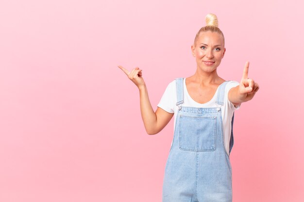 Pretty blond woman smiling and looking friendly, showing number one