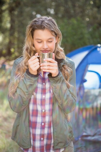 Pretty blonde camper enjoying beverage in front of tent