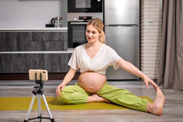Pretty blonde caucasian pregnant woman do yoga exercises watching video online
