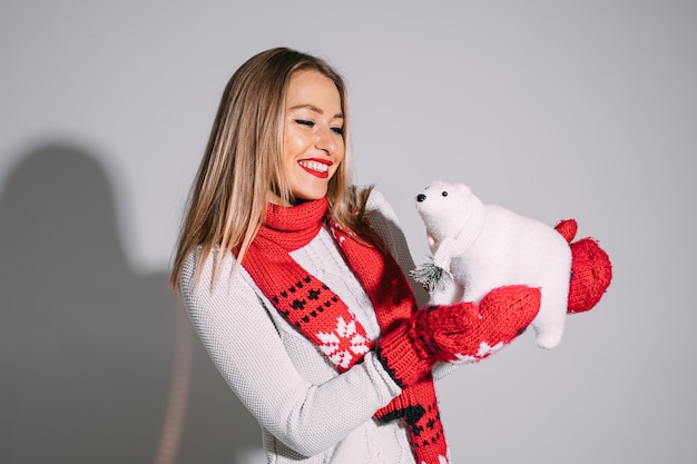  pretty blonde Caucasian woman in mittens and scarf and white sweater holding cute white toy bear and smiling.