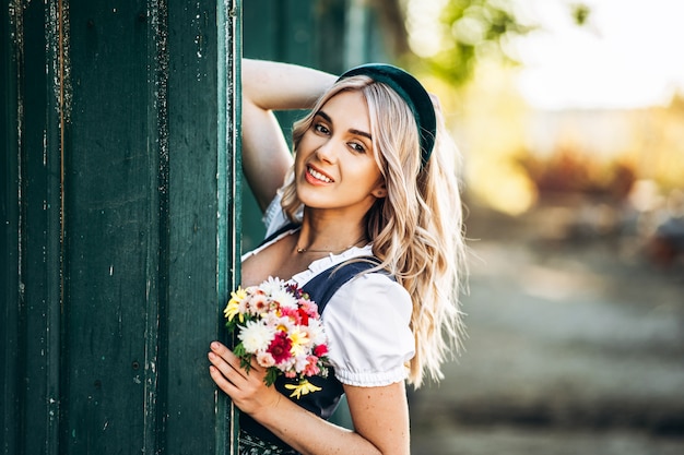 Довольно блондинка в дирндль, традиционное платье Октоберфест стоя на ферме возле деревянной двери