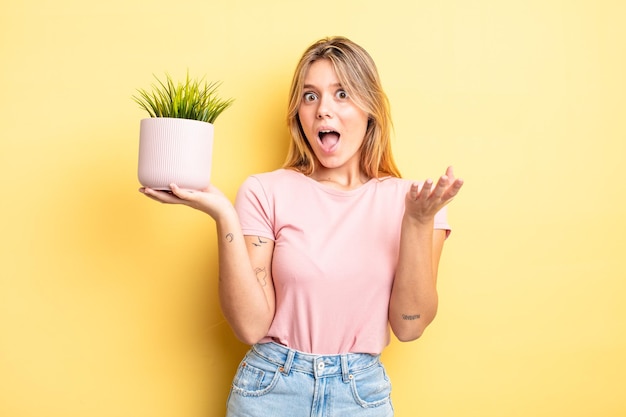 Pretty blonde girl amazed, shocked and astonished with an unbelievable surprise. houseplant concept