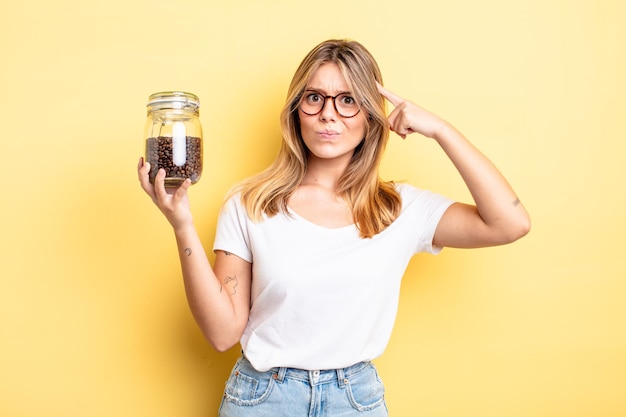 Pretty blonde girl feeling confused and puzzled, showing you are insane. coffee beans concept