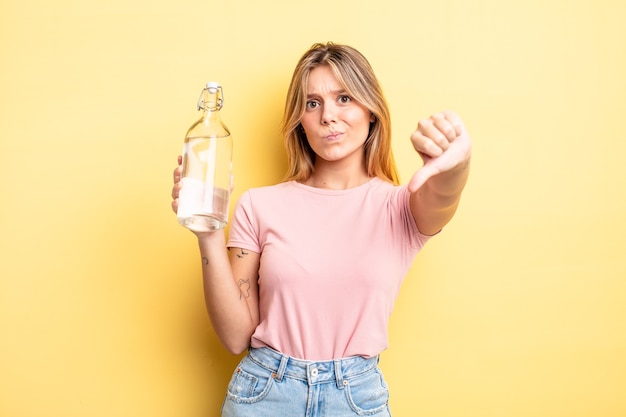 Bella ragazza bionda che si sente croce, mostra i pollici in giù. concetto di bottiglia d'acqua