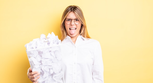 Bella ragazza bionda che si sente disgustata e irritata e con la lingua fuori. concetto di spazzatura delle palle di carta